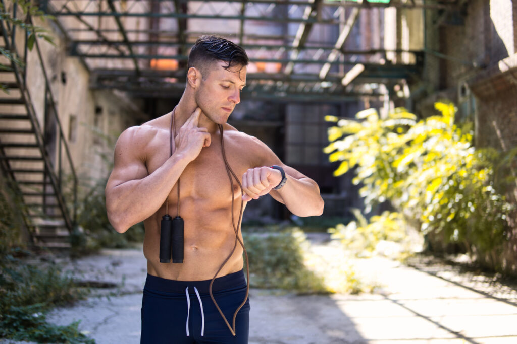 Handsome muscular sportsman training with jumping rope outdoors.